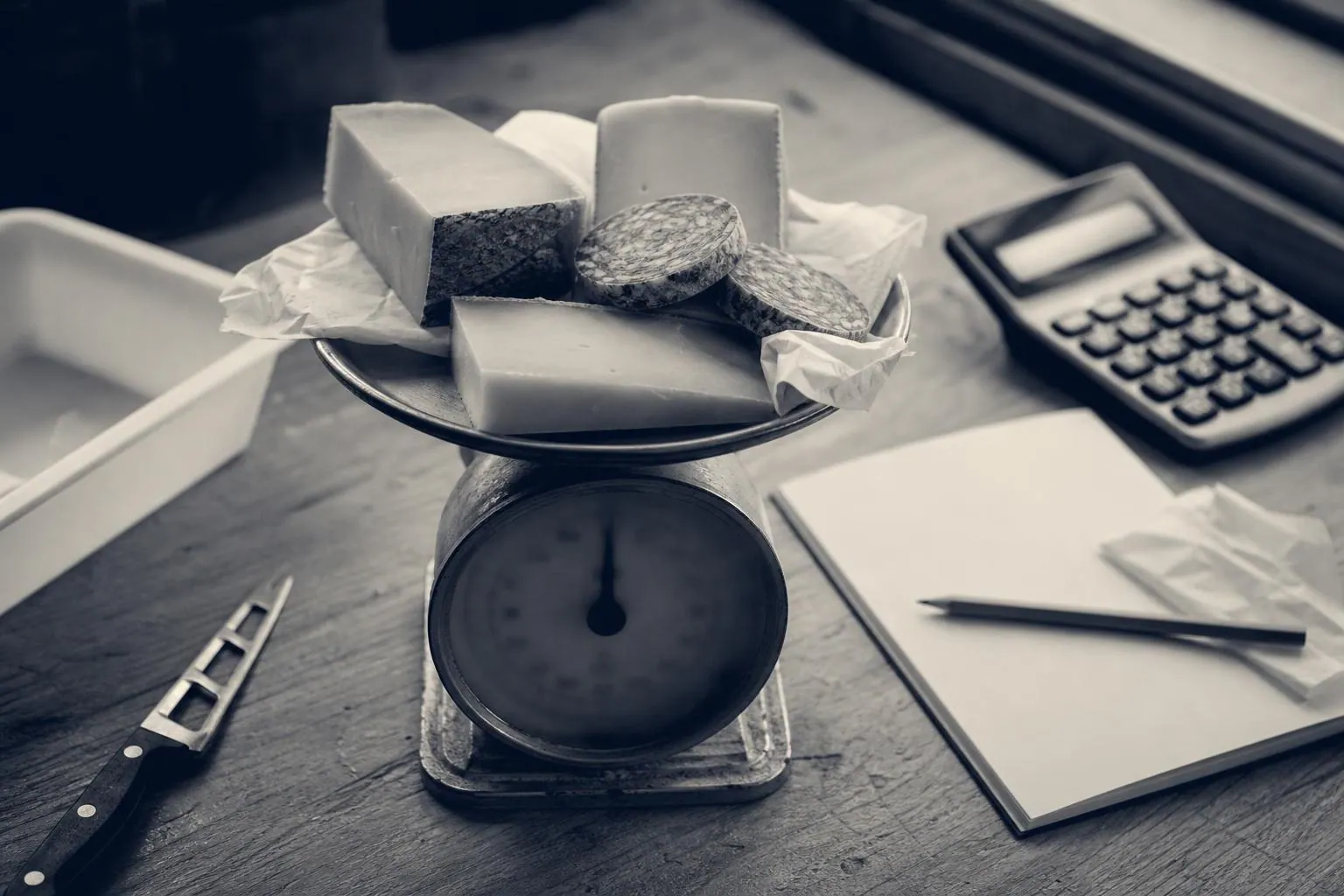 Balance de comptoir supportant des morceaux de fromage retires de la vente, posee pres d un carnet et d une calculatrice sur un plan de travail
