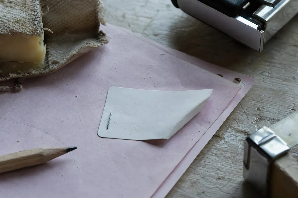 Gros plan d une etiquette adhesive de lot agrafee sur un bon de livraison en papier, posee a cote d une croute de fromage a pate pressee et d un crayon de bois